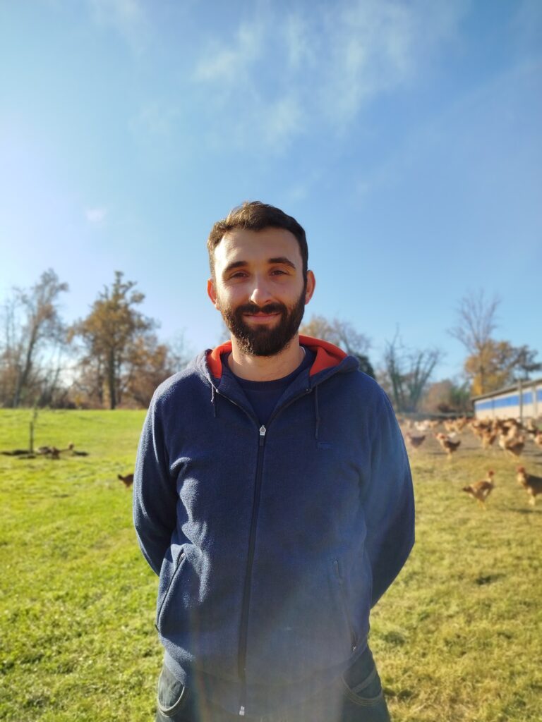 Un champs, des volailles en arrière plan, un agriculteur au premier plan